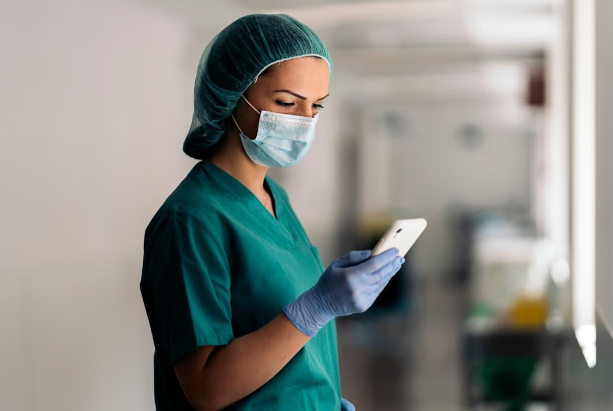 A healthcare professional in blue scrubs uses a smartphone