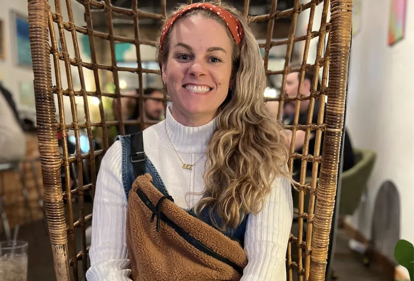 Smiling nurse seated in a wicker chair in a casual setting.