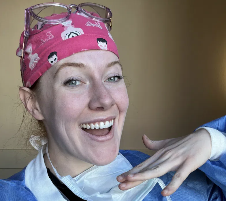 Nurse wearing protective gear and a surgical cap smiling at work.