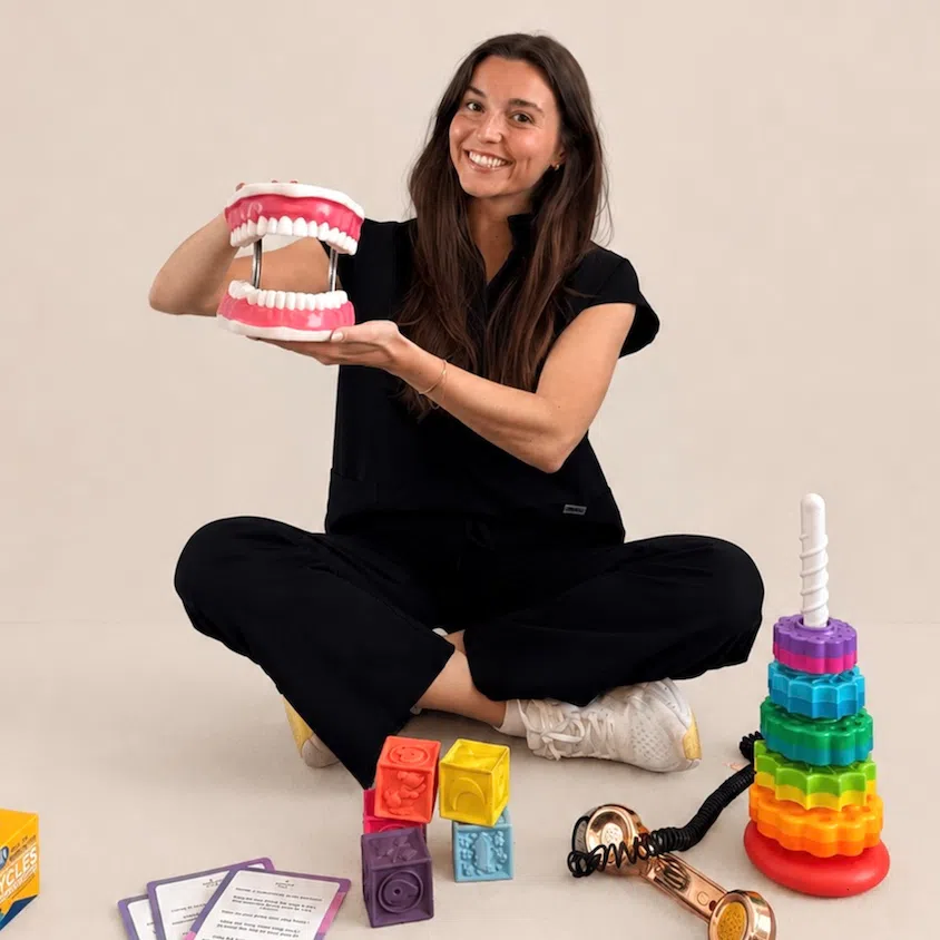 Kaitlyn, an SLP in New York, holding a speech therapy mouth model with therapy tools nearby